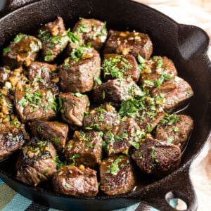 Steak bites garnished with parsley in a cast iron skillet.