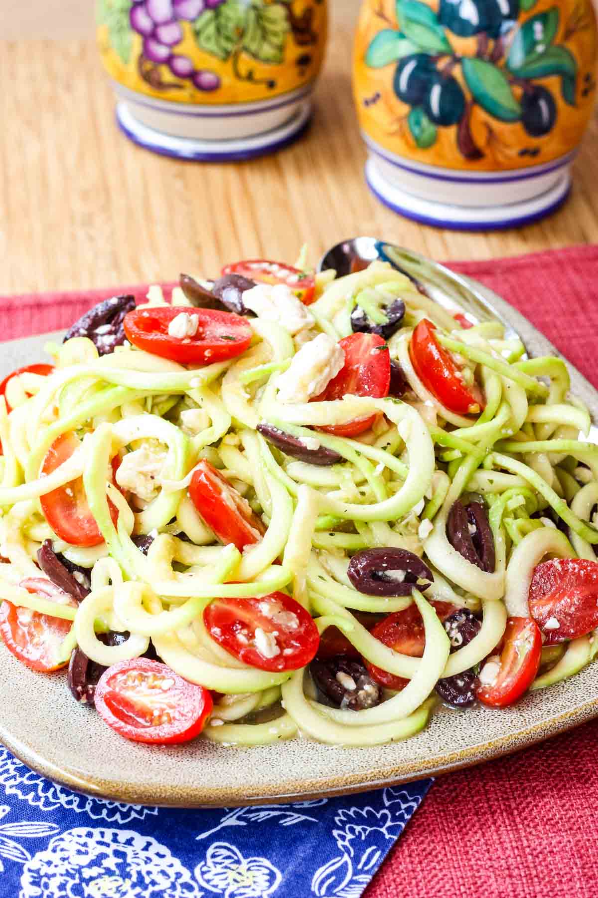 A plate of Greek zoodle salad on a table.