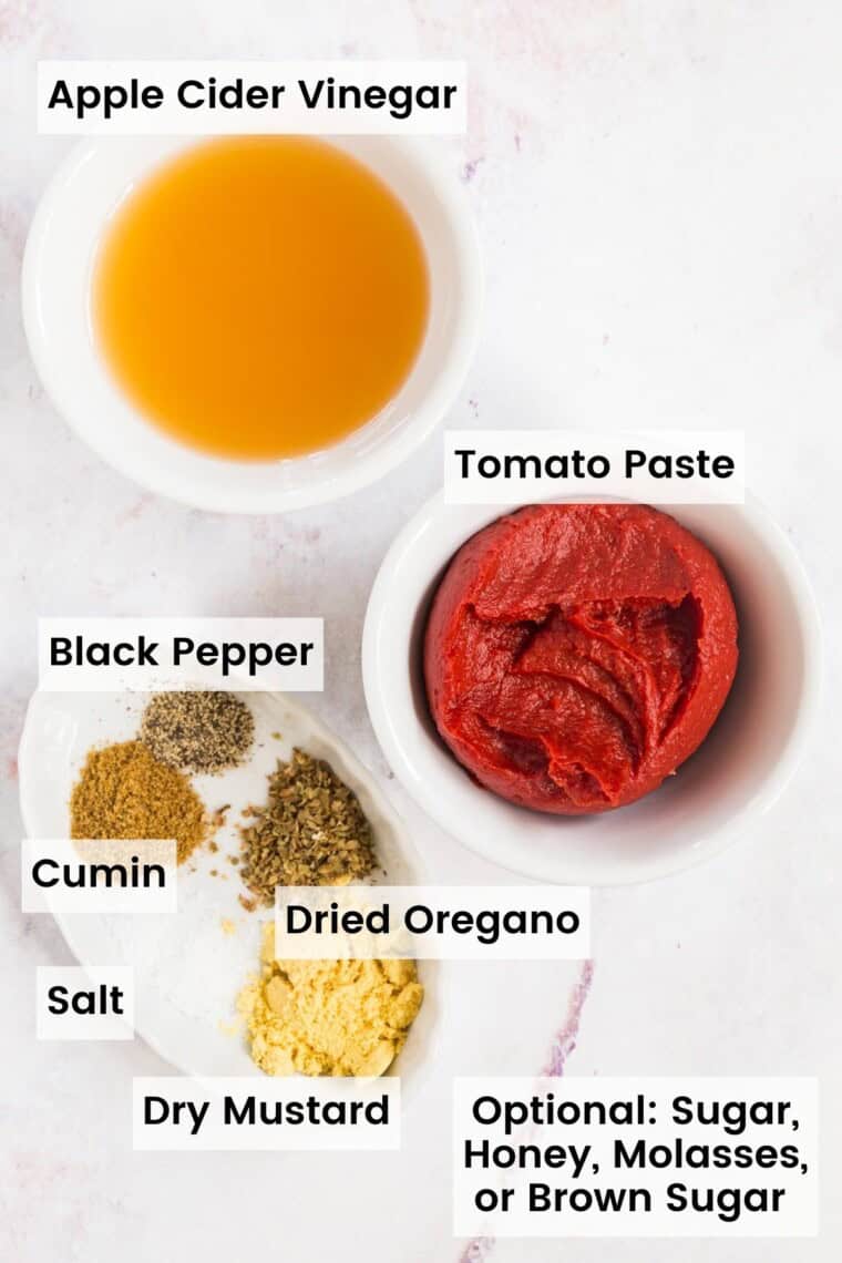 The ingredients to make homemade ketchup in bowls with text labels, including Apple Cider Vinegar, Tomato Paste, Black Pepper, Cumin, Salt, Dried Oregano, and Dry Mustard.