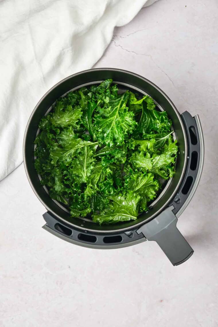 The kale is added to a air fryer basket.