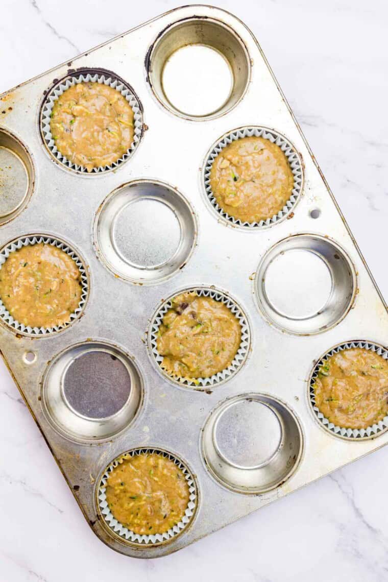 The batter is added to the muffin tin, filling half of the cups and leaving the other half empty.