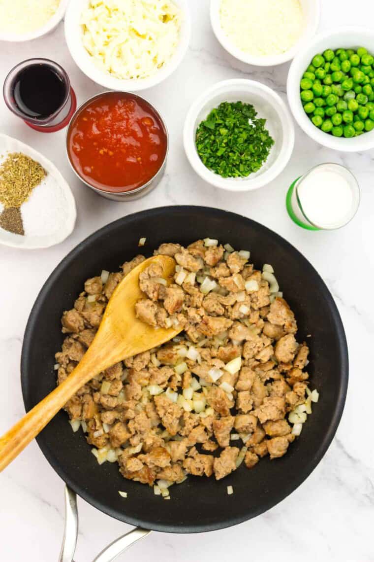 A wooden spoon stirring a pan of cooked sausage and chopped onion.