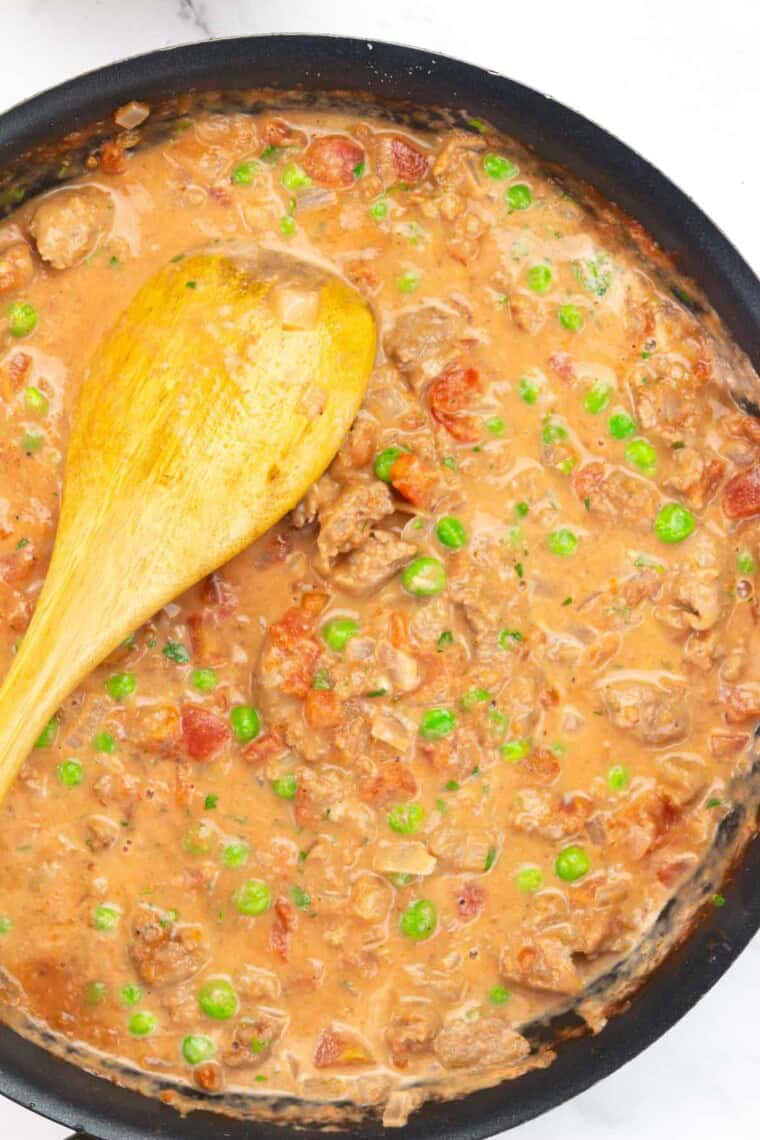 Creamy tomato and sausage sauce in a pan with a wooden spoon.