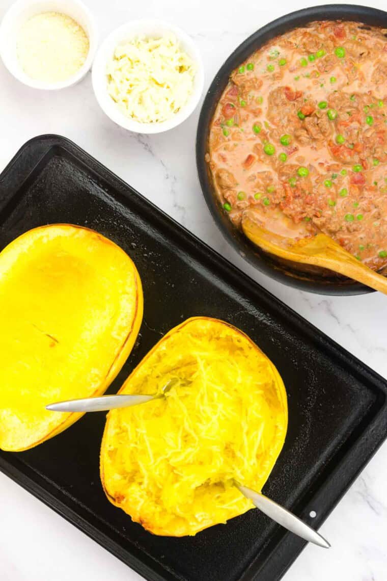 Two forks separating the noodles of a spaghetti squash and the pan of meat sauce next to it.