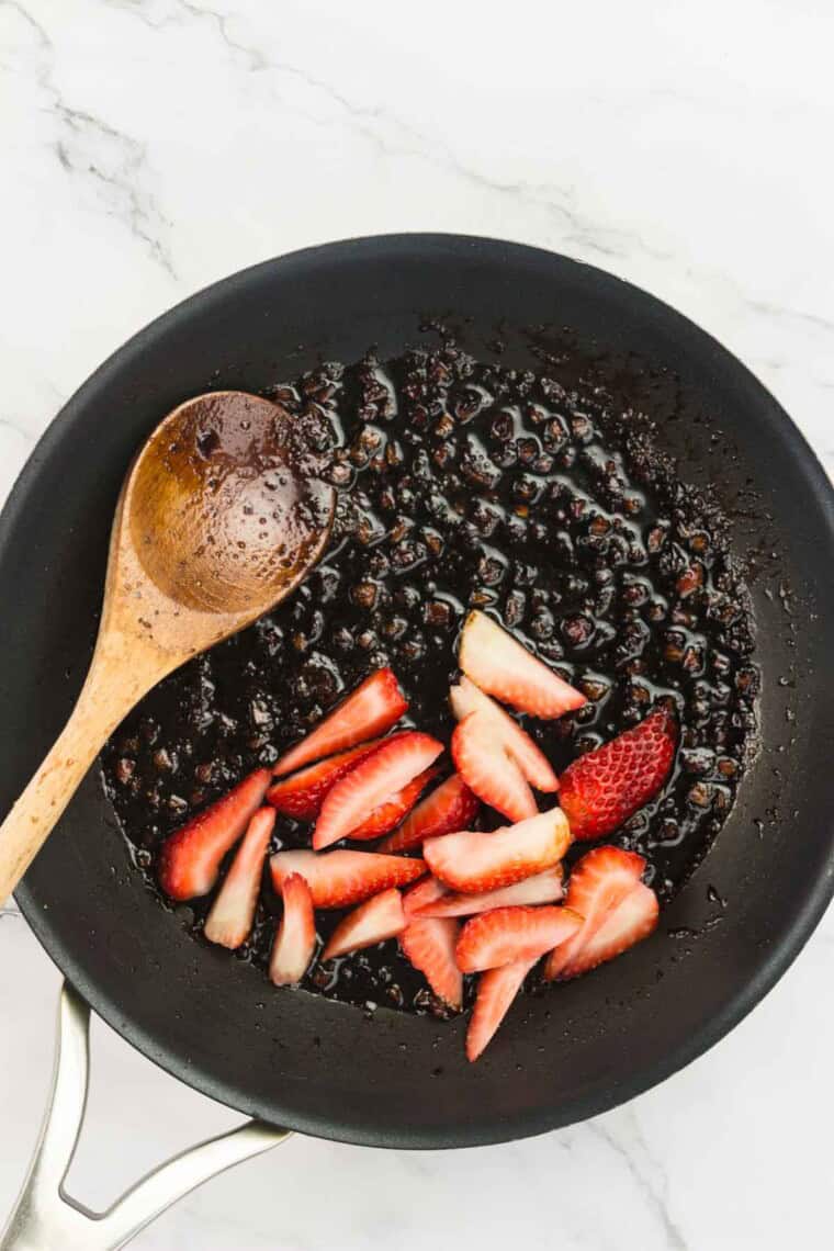 Sliced strawberries are added to the vinegar in the pan.