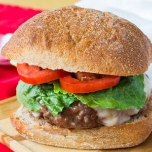 An Italian burger topped with cheese, tomato and lettuce on a bun.