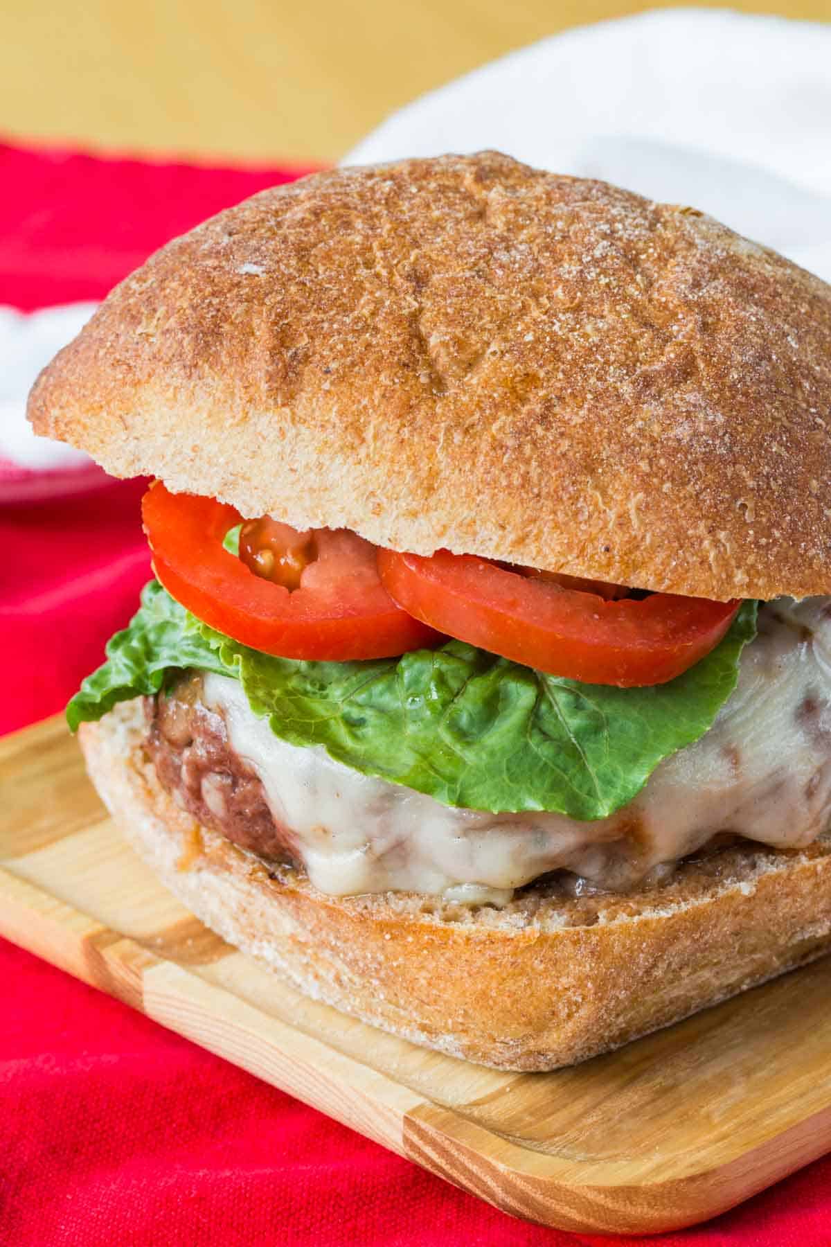 An Italian burger topped with cheese, tomato and lettuce on a bun.