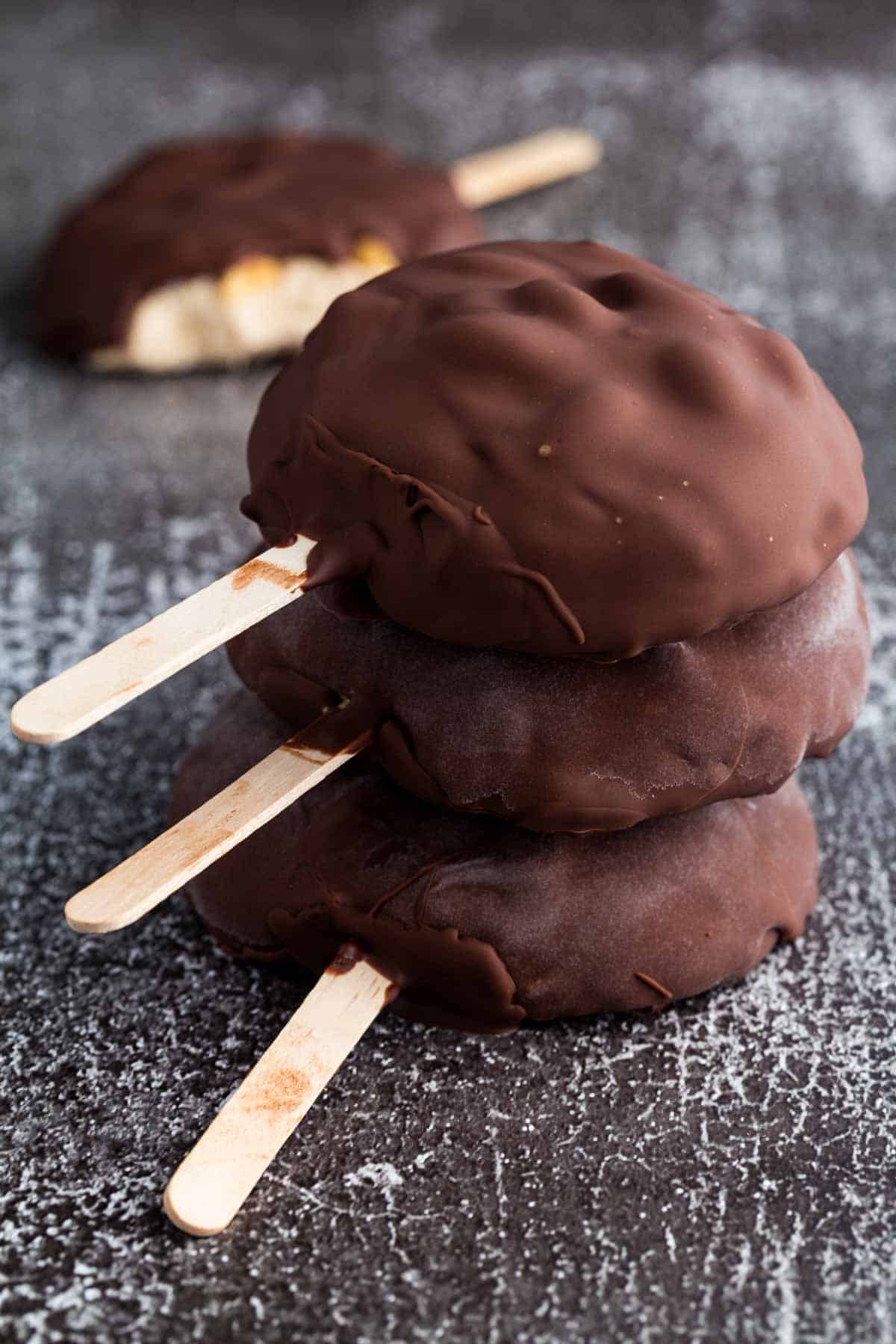 Chocolate covered peanut butter frozen yogurt bars with popsicle sticks are stacked on top of one another.