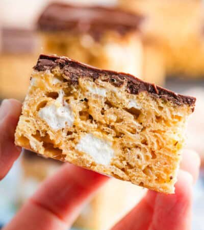 A close up of a hand holding a peanut butter rice krispies treat showing marshmallows inside.