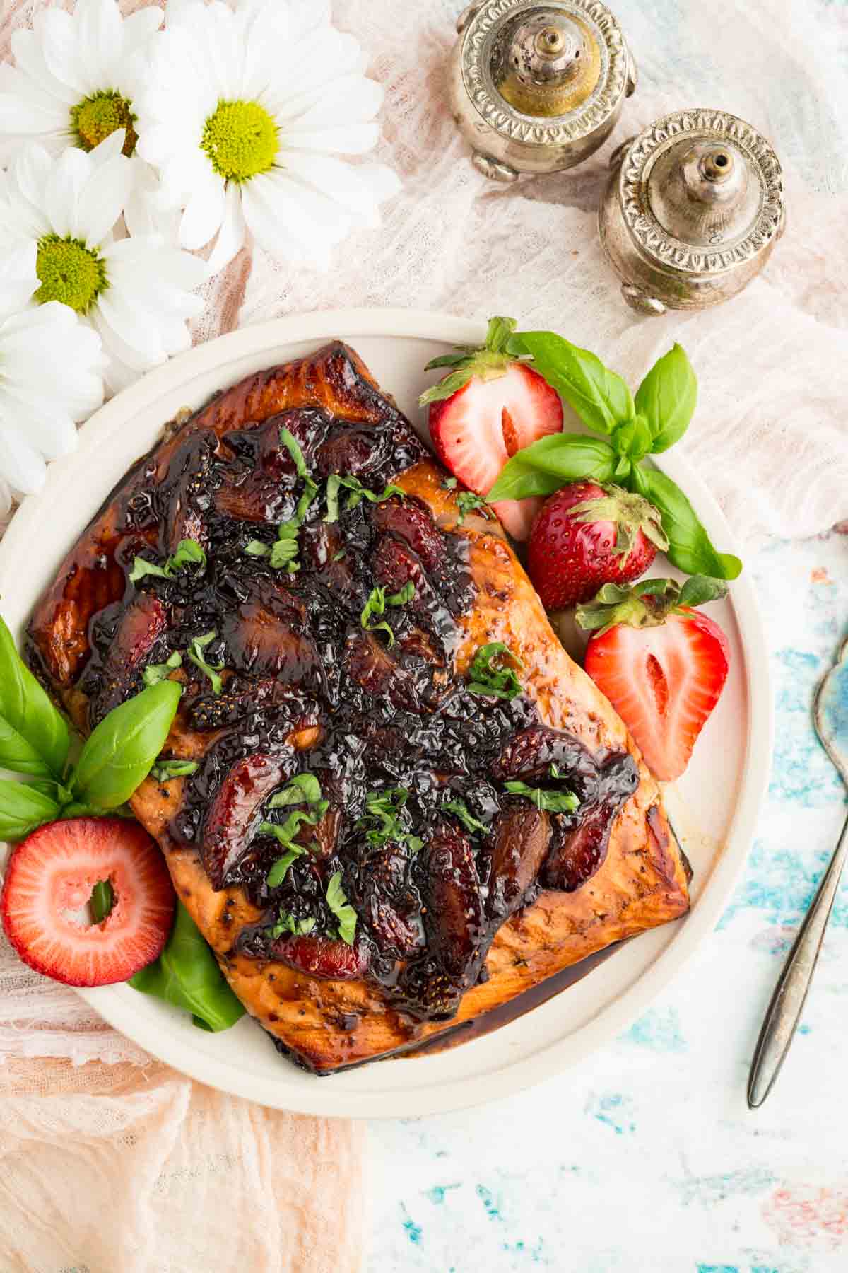 A top down view of a large piece of balsamic salmon with strawberries.