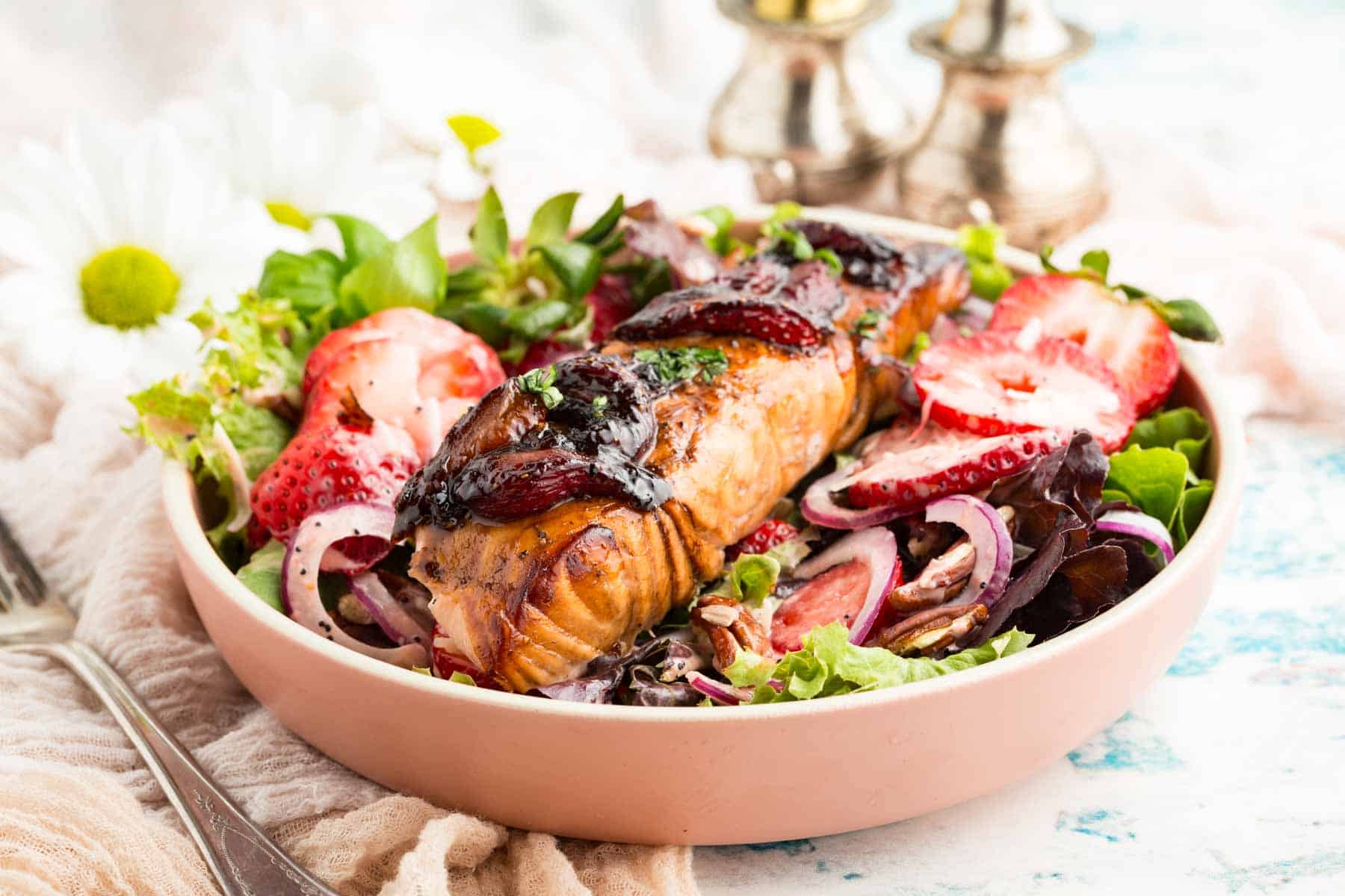 A balsamic-glazed piece of salmon is served in a bowl with strawberries and broccoli.