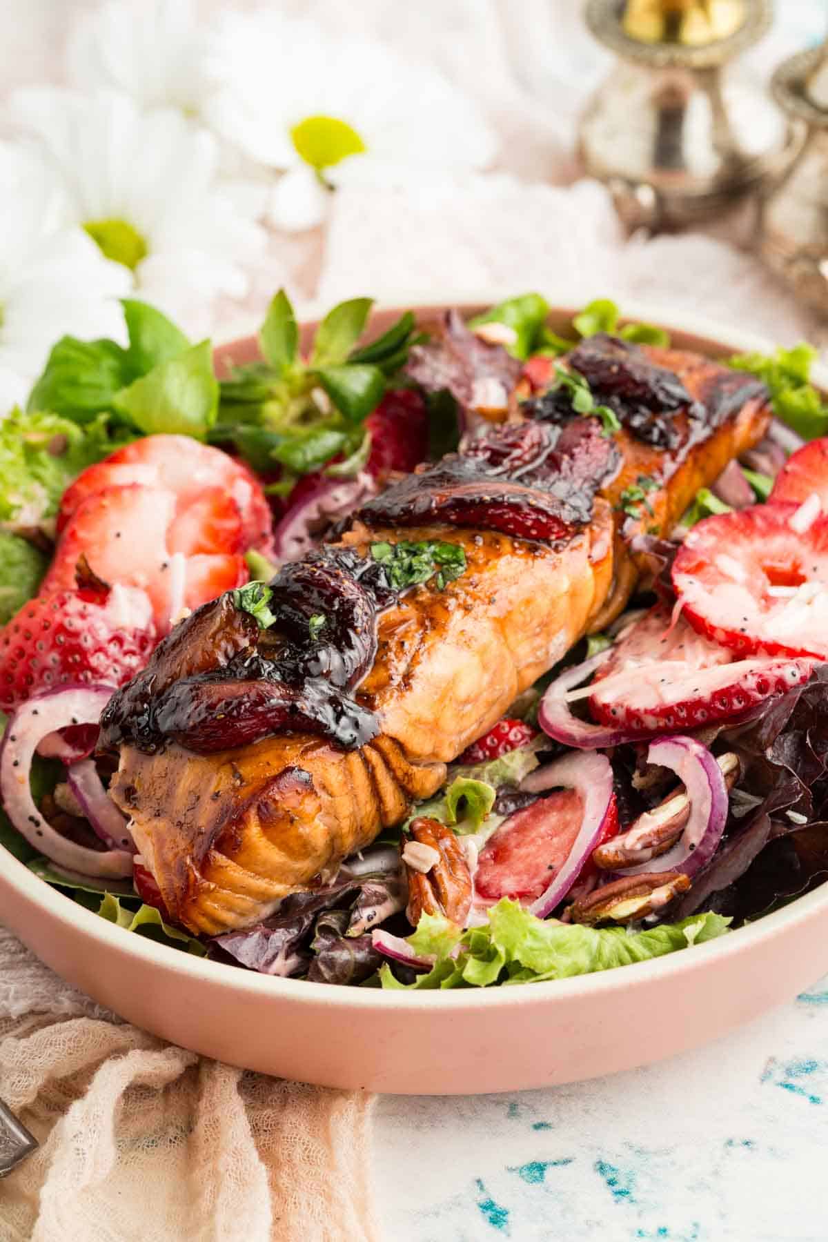 A balsamic-glazed piece of salmon is served in a bowl with strawberries and broccoli.