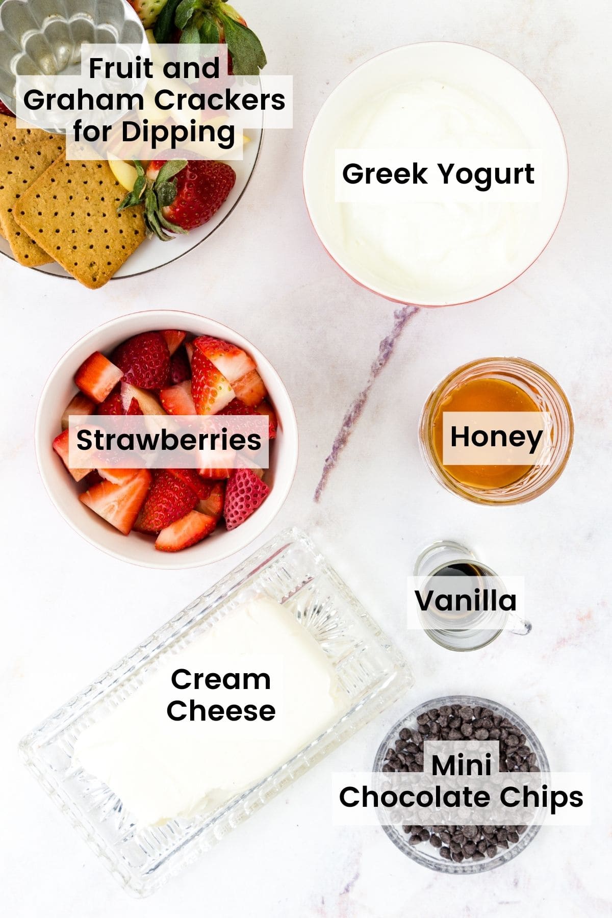 The ingredients for strawberry fruit dip are shown with text labels: strawberries, honey, cream cheese, Greek yogurt, vanilla extract, chocolate chips.