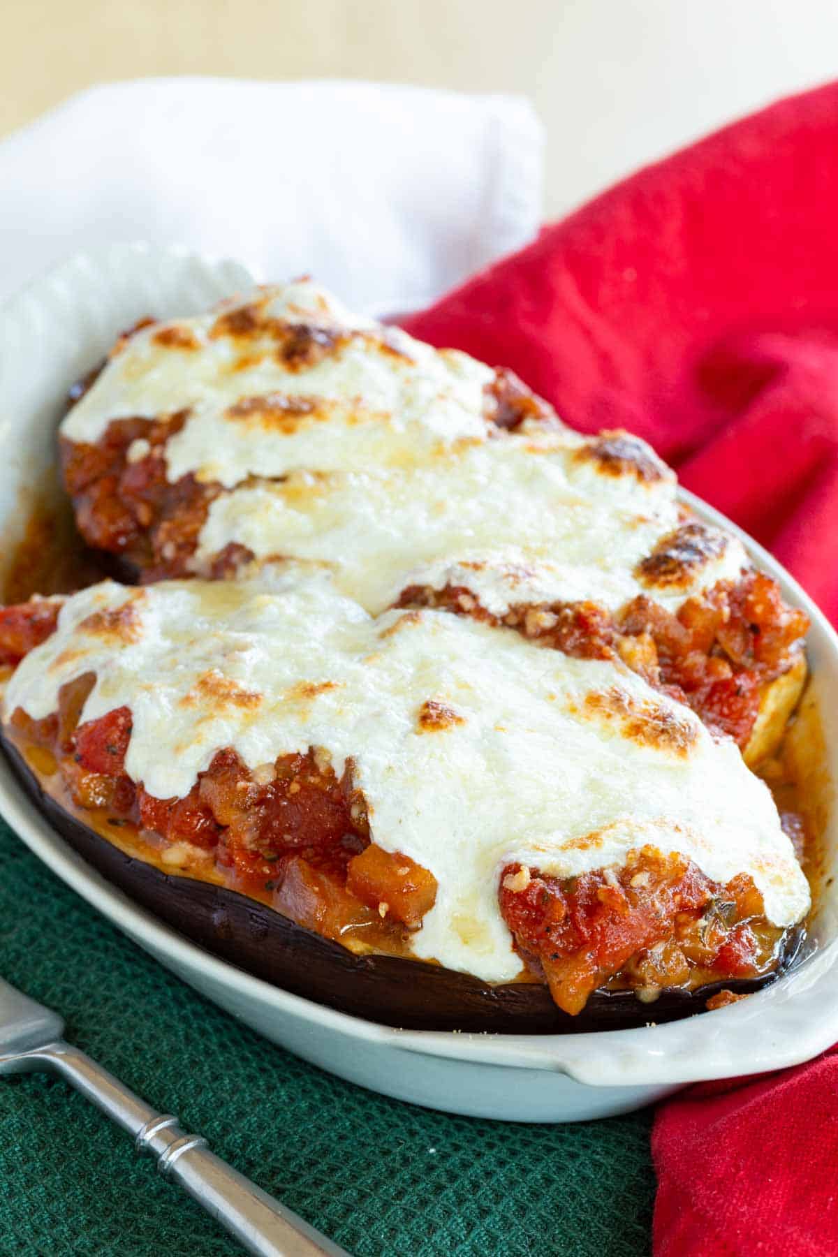 A serving dish holds two pieces of stuffed eggplant topped generously with melted mozzarella.