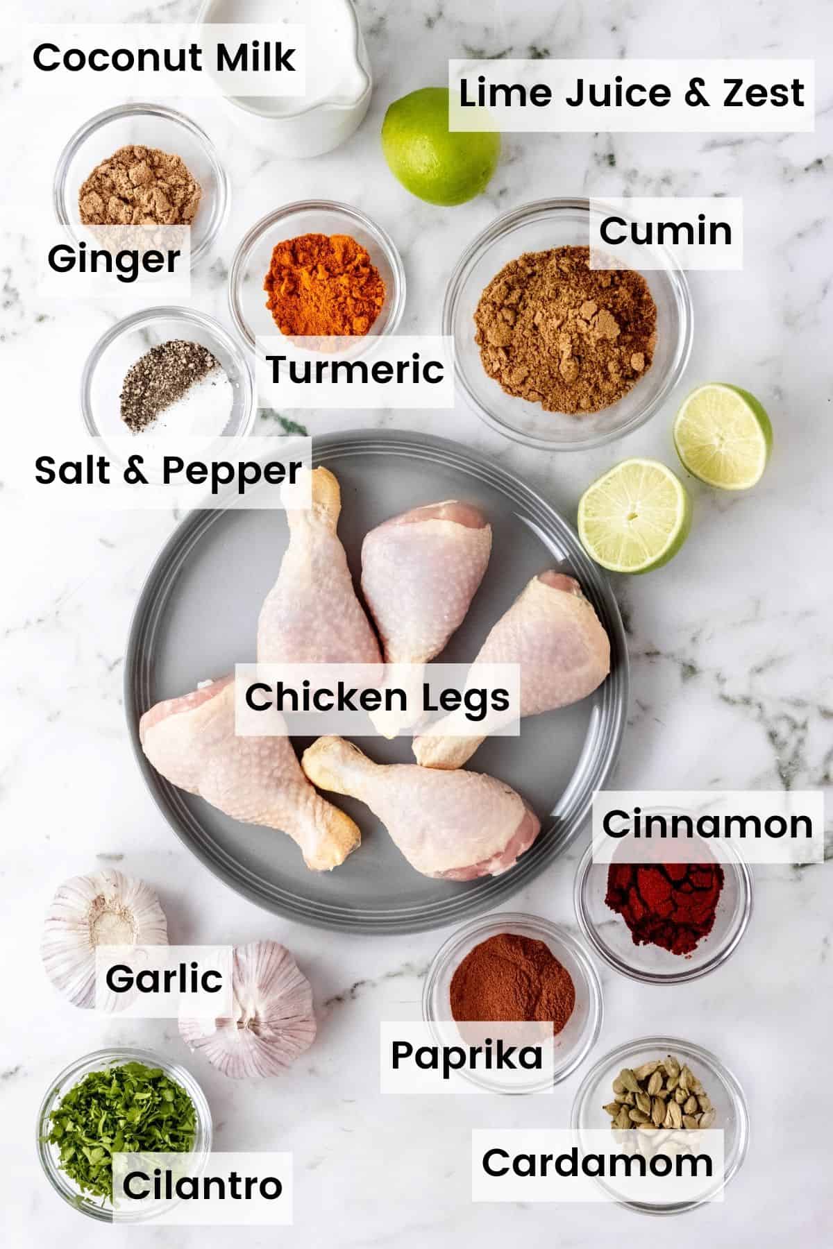 Ingredients needed to make tandoori chicken with text labels: Coconut milk, lime juice and zest, ginver, cumin, turmeric, salt and pepper, chicken legs, cinnamon, garlic, paprika, cardamom, and cilantro.