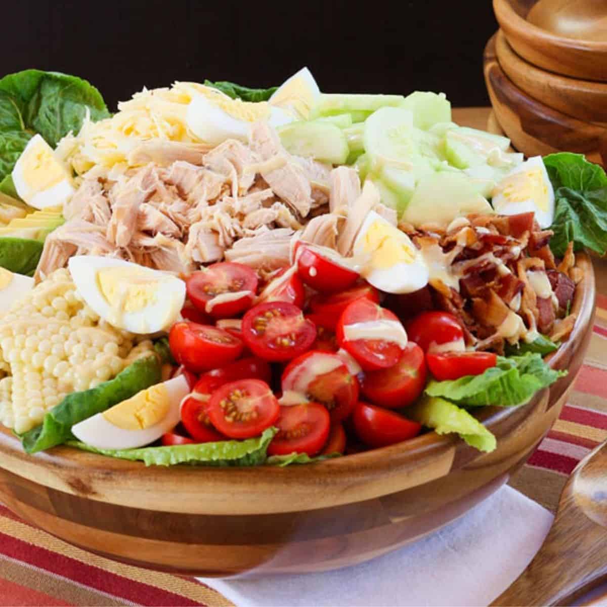 A chicken cobb salad overflowing from a wooden salad bowl.