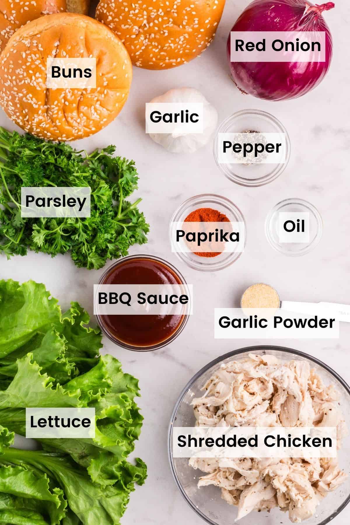 The ingredients for bbq chicken sandwiches are shown labeled and portioned: chicken, buns, garlic, red onion, garlic, lettuce, bbq sauce, oil, paprika, pepper, garlic powder.