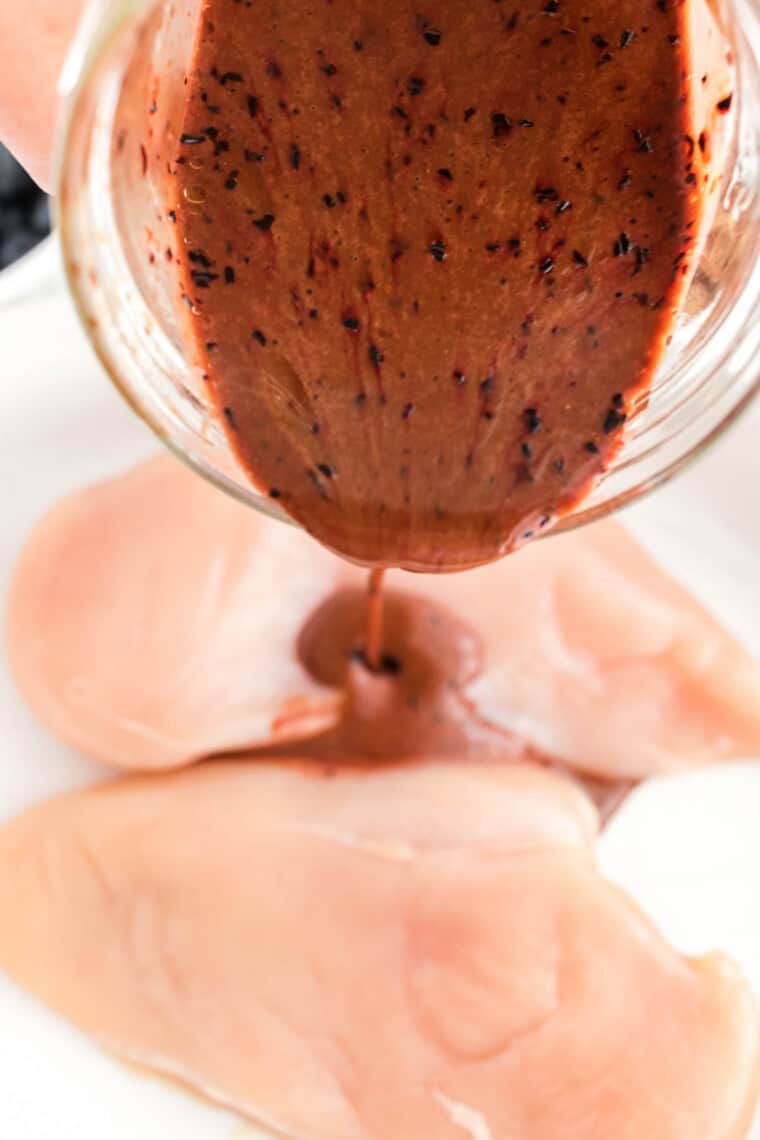 Blueberry balsamic marinade being poured over raw chicken breasts.