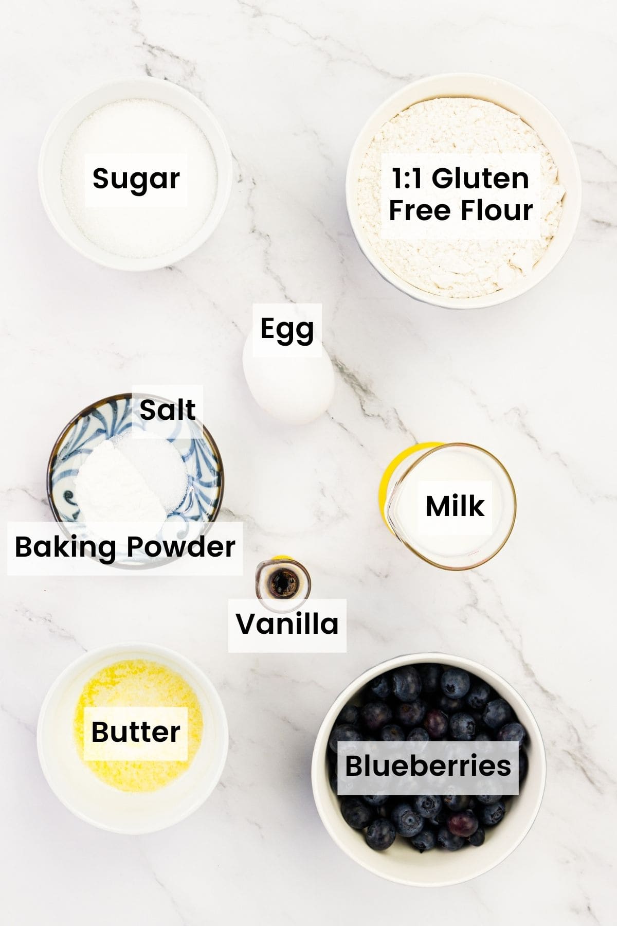 Gluten free blueberry donut ingredients are shown labeled: baking powder, sugar, egg, gluten free flour, butter, vanilla, milk, blueberries.