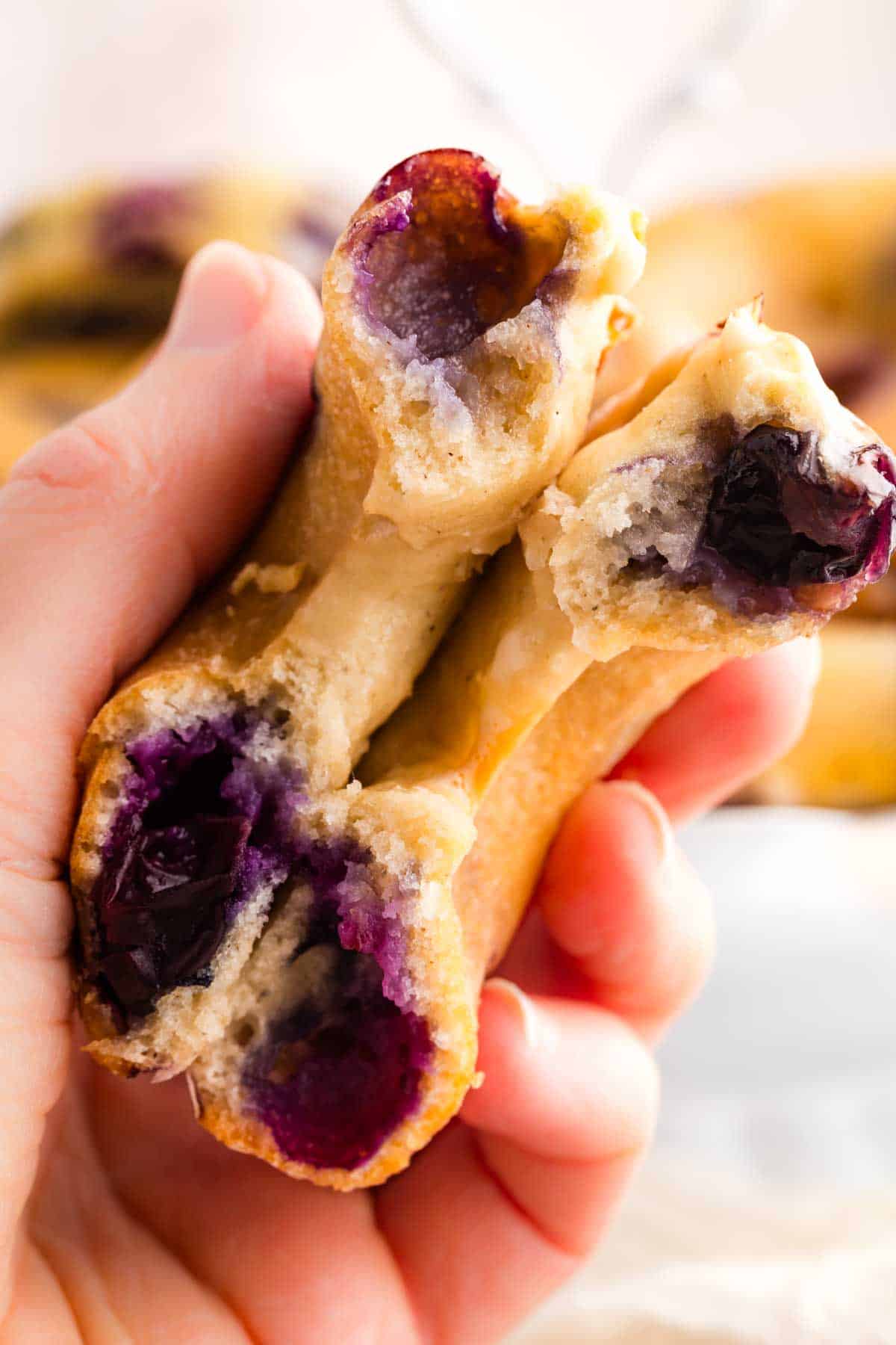 A hand holds two blueberry-stuffed halves of a blueberry donut.