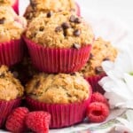 Gluten free raspberry muffins are piled on a plate with fresh raspberries scattered around them.