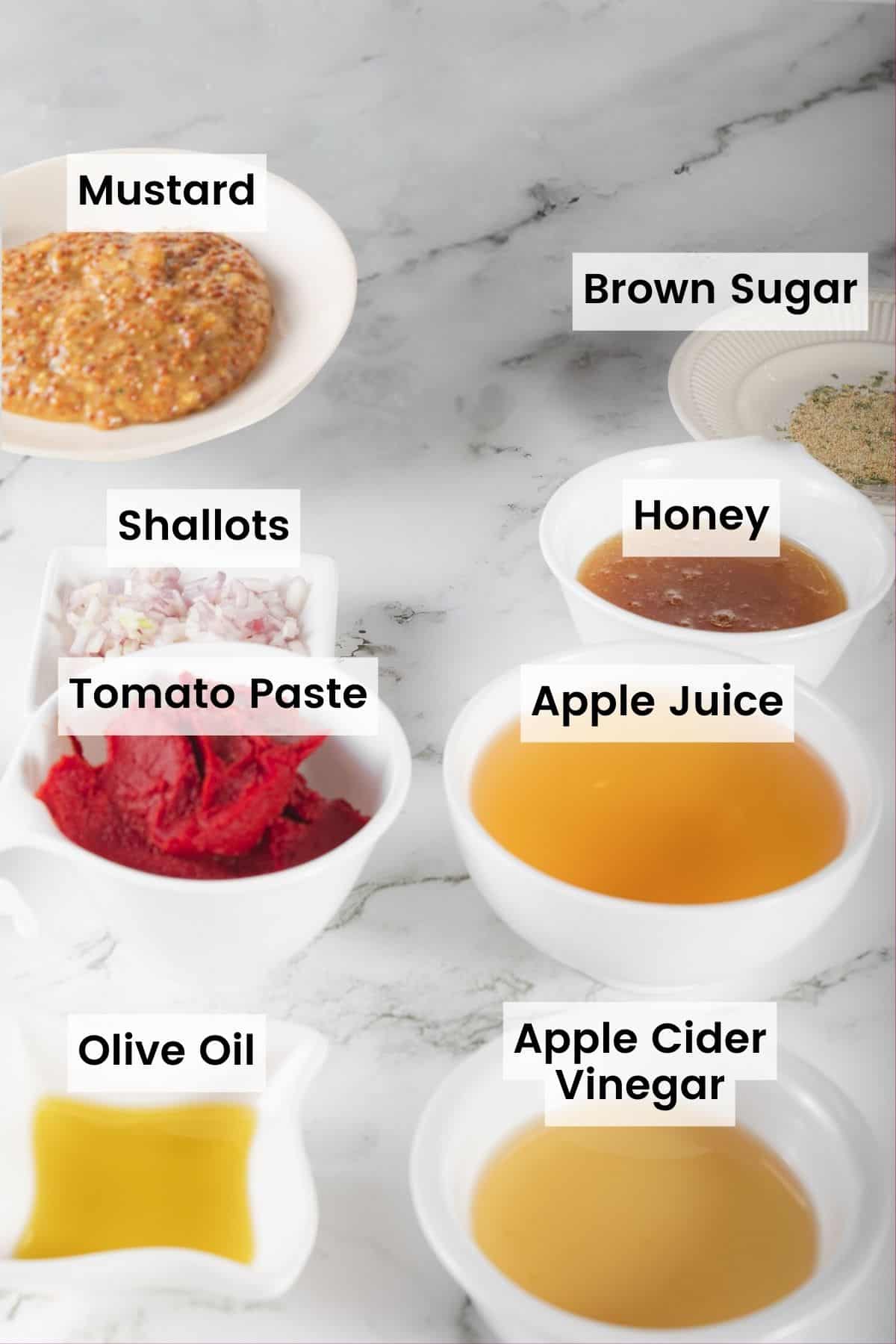 Ingredients to make honey barbecue sauce in bowls on a countertop with text labels including: Mustard, Brown Sugar, Shallots, Honey, Tomato Paste, Apple Juice, Olive Oil, and Apple Cider Vinegar.