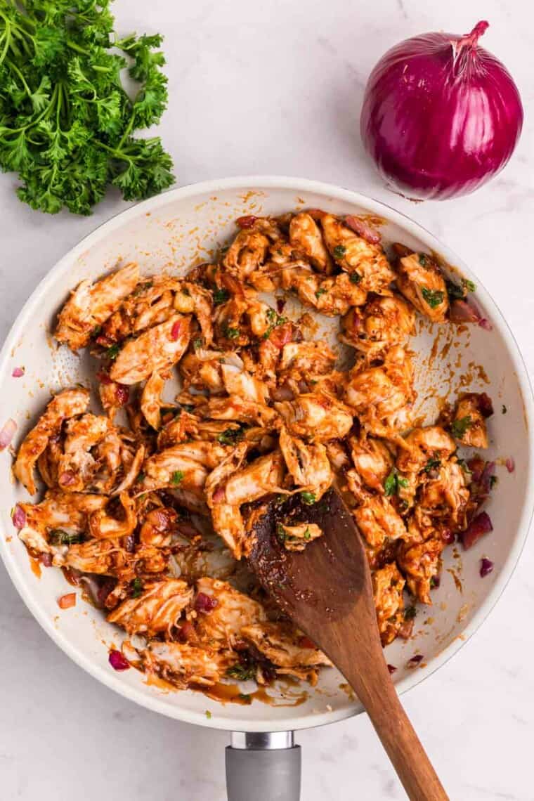 A spoon stirs the filling ingredients together in a bowl for bbq chicken.