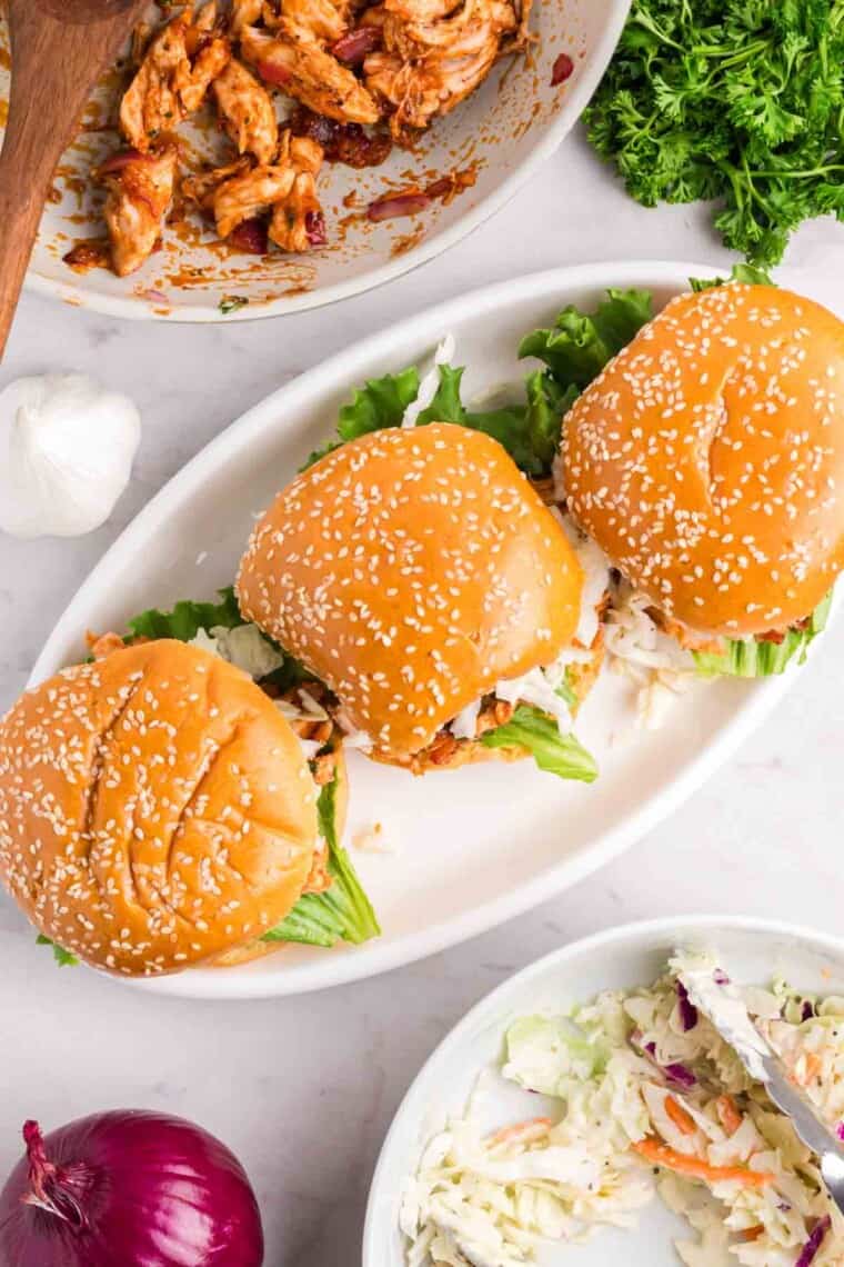 A white oval serving holds three bbq chicken sandwiches.