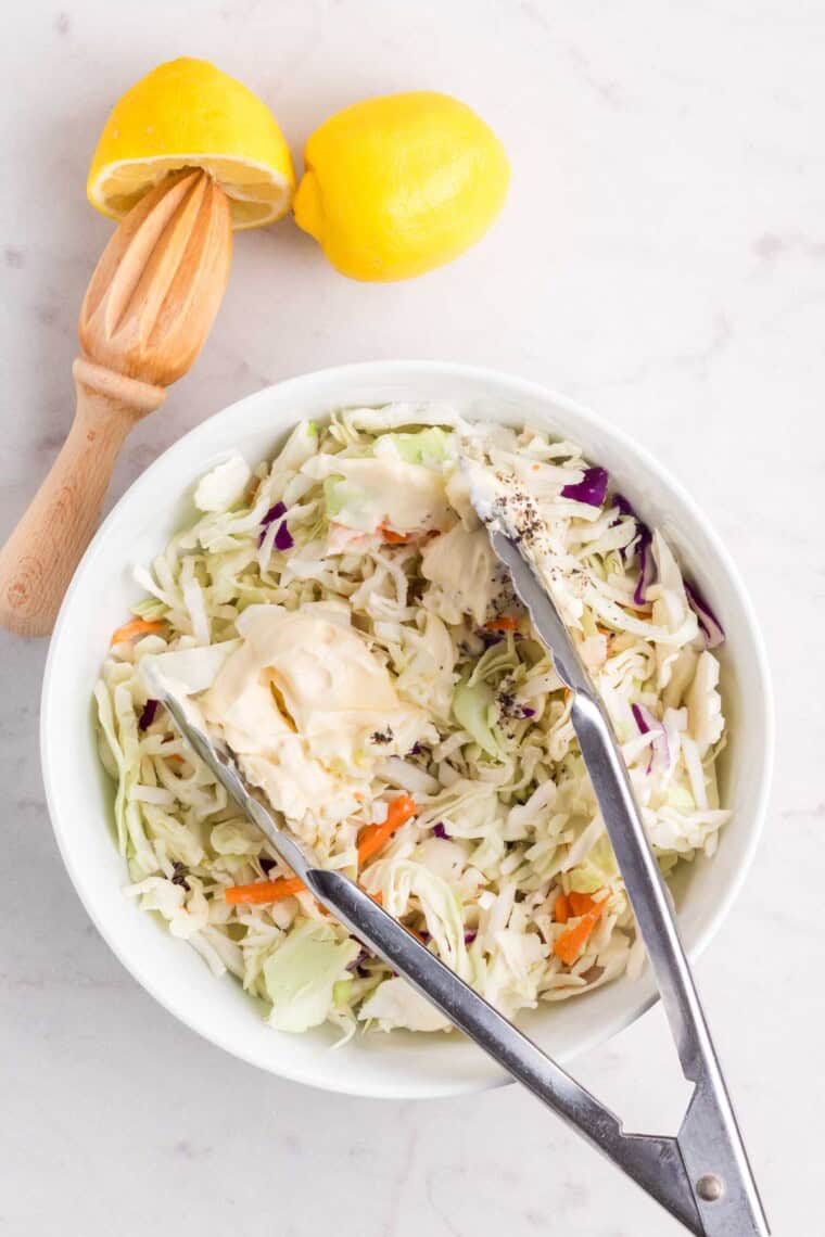 Tongs are used to mix the mayonnaise into the coleslaw mix.