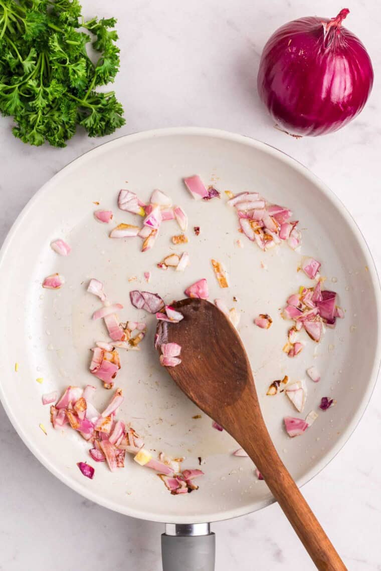 A spoon stirs diced red onion in a skillet.