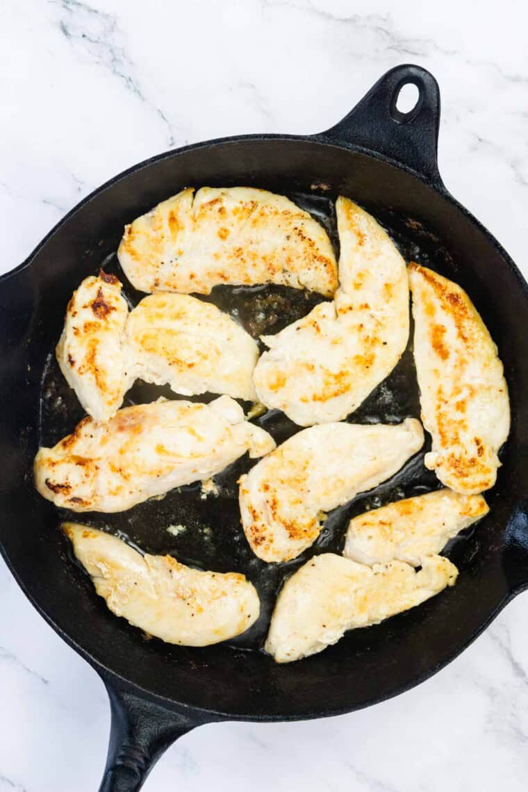 Chicken tenders cook in a cast iron skillet.