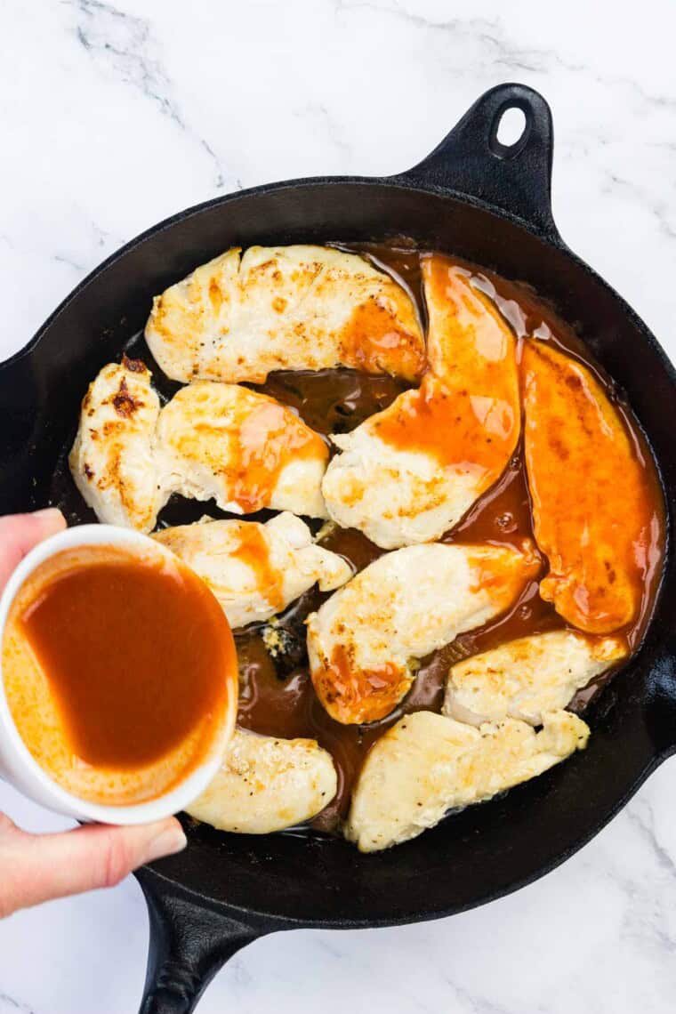 Hot sauce is poured over chicken tenders in a cast iron skillet.