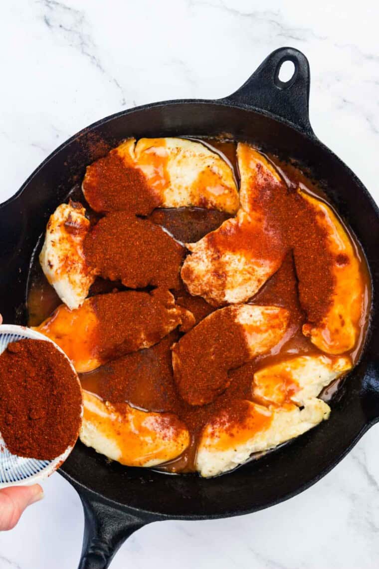 Half of the paprika is added to the chicken in the skillet.