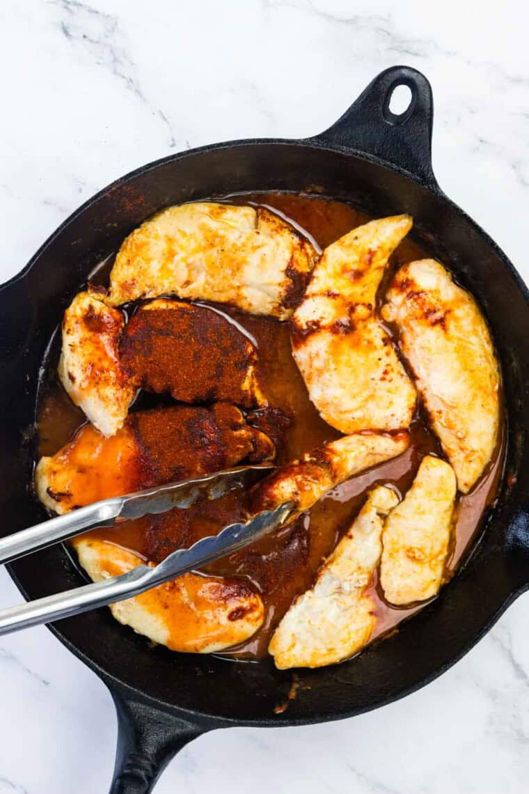 Tongs mix in the seasonings to the skillet.