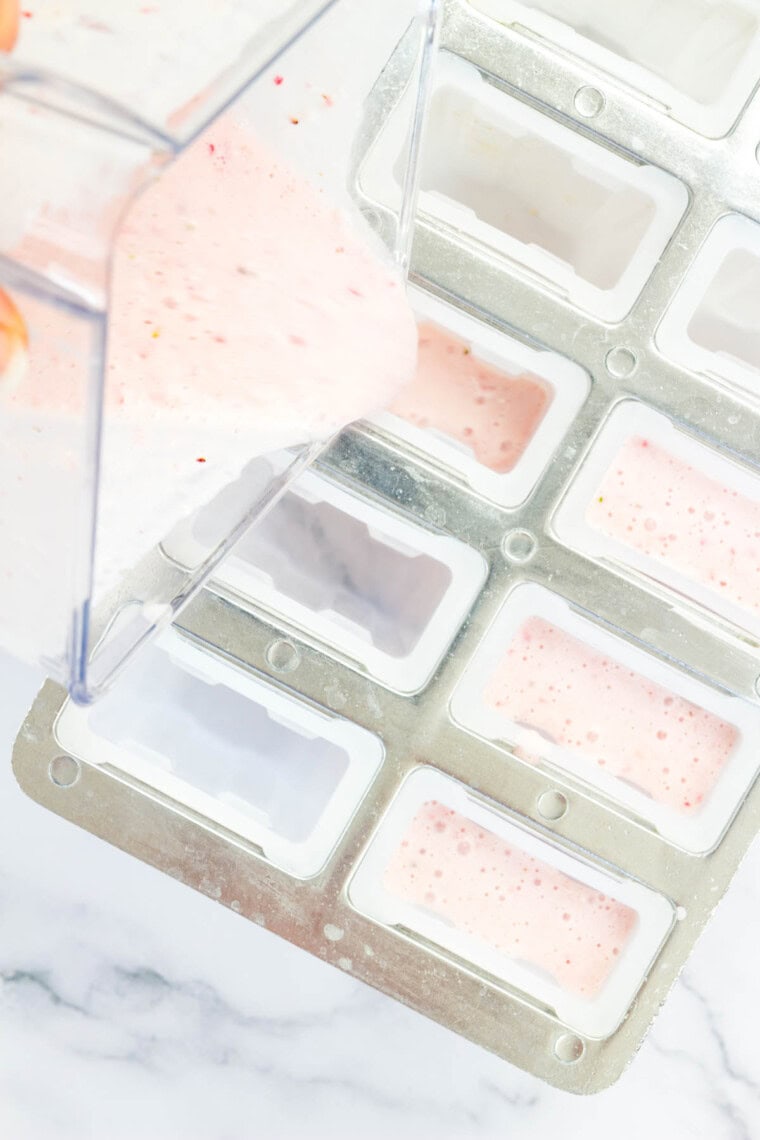 The pink strawberry yogurt popsicle mixture being poured into a mold.