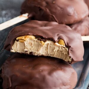 Peanut butter frozen yogurt bars covered in chocolate coating on a tray with a few bites taken out of one.