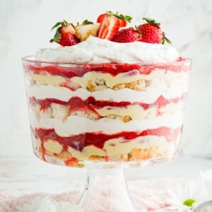 A strawberry shortcake trifle in a glass bowl pedestal bowl to show the layers of cake, custard, berries, and whipped cream.