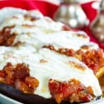 Two eggplant halves filled with sauce and cheese in a white dish with text overlay that says "Stuffed Eggplant Parmesan".