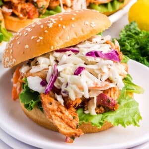 A barbecue chicken sandwich topped with coleslaw on a plate.