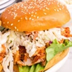 A barbecue chicken sandwich with coleslaw on a sesame seed bun with text overlay that says "BBQ Chicken Sandwiches".