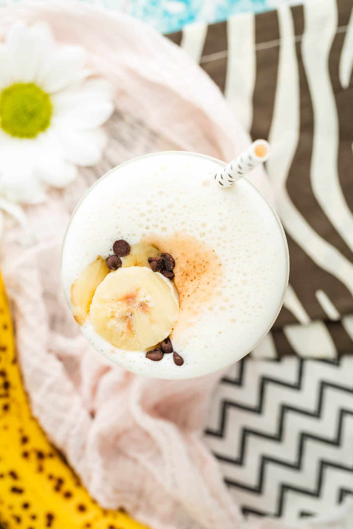 A top down view of a glass of banana smoothie topped with banana slices and chocolate chips.