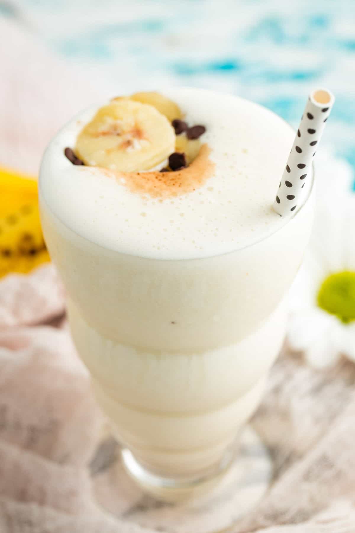 A creamy banana smoothie is served in a tall glass with a straw.