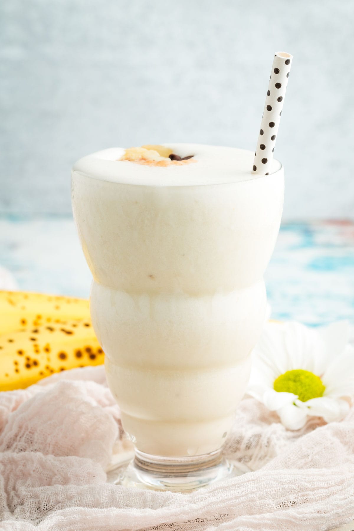 A tall glass holds a banana smoothie with a straw sticking out of it.