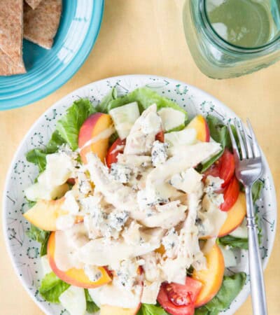 A birds-eye view of the chicken peach salad on a plate with a glass of water and plate of pita next to it.