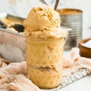 A glass jar holds scoops of homemade dulce de leche ice cream with a spoon.