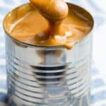 A caramel-colored sauce dripping off a spoon into a can with text overlay that says "Dulce de Leche".