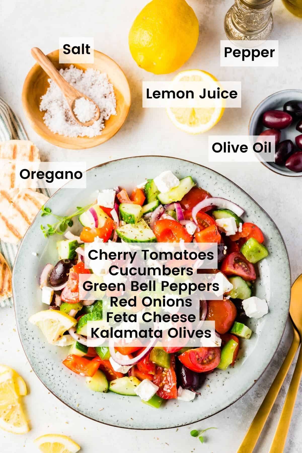 A bowl of Greek salad with some of the ingredients on the countertop with text labels that say: Salt, pepper, lemon juice, olive oil. oregano, cherry tomatoes, cucumbers, green bell peppers, red onions, feta cheese, and kalamata olives.