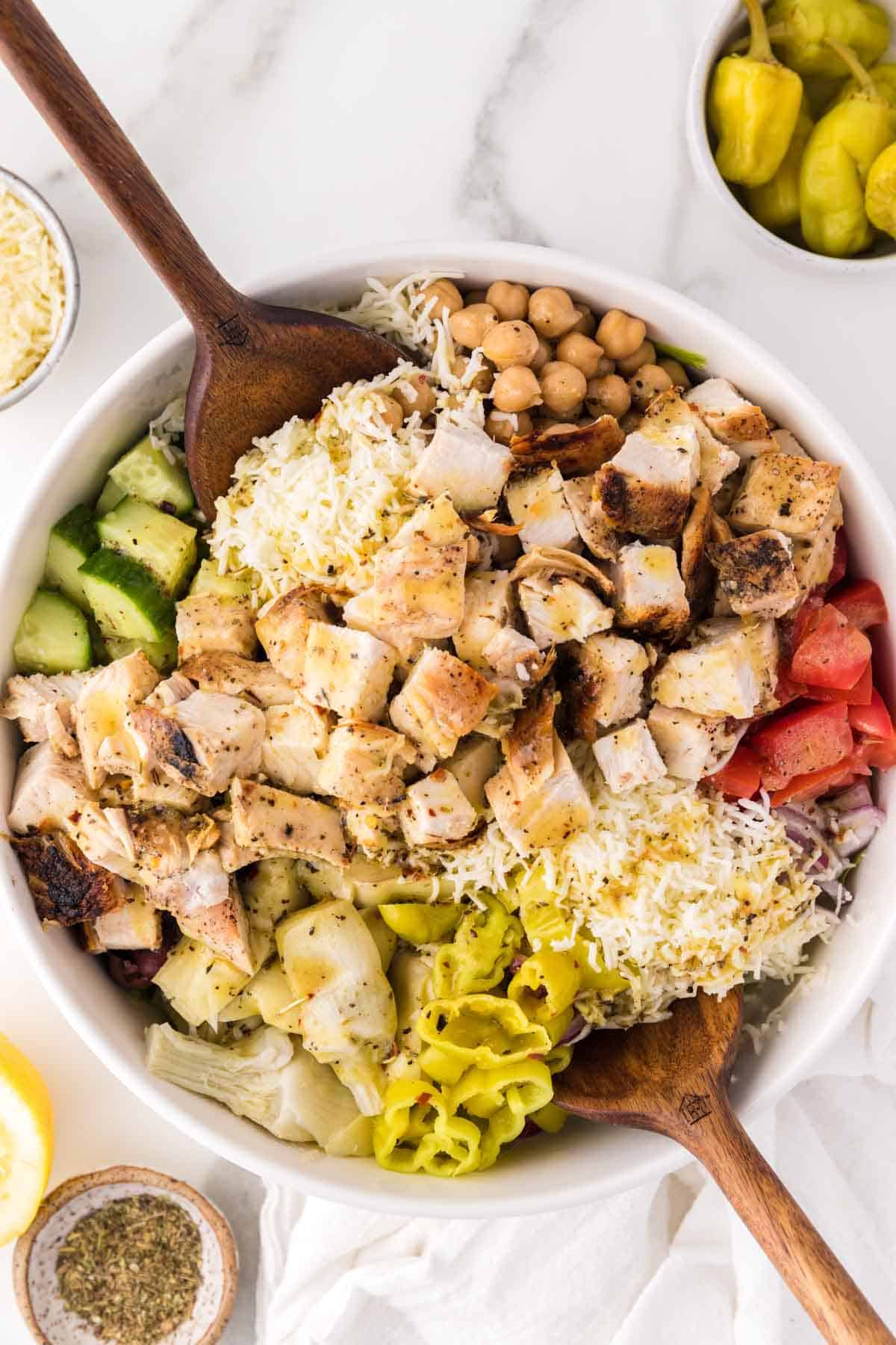 A large bow of Italian chopped salad with two salad utensils is served on a table.