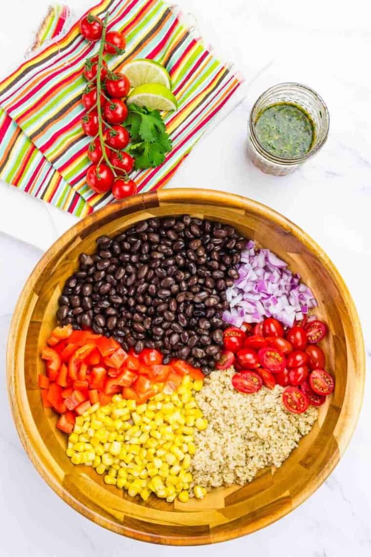 The components of Mexican quinoa salad are added to a bowl.