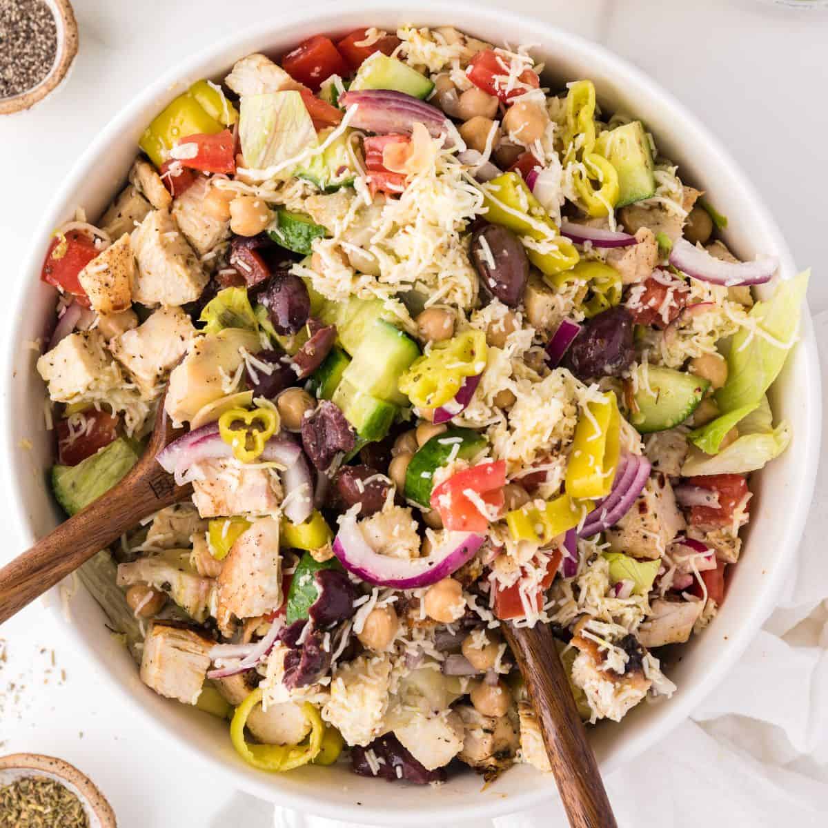 Two salad spoons mix a bowl of Italian chopped salad.